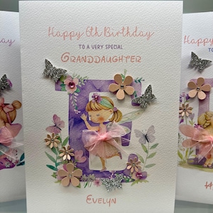 May include: A purple and white card with a pink and white fairy illustration and the text "Happy 6th Birthday to a very special Granddaughter Evelyn". The card is decorated with glitter butterflies, flowers, and rhinestones.