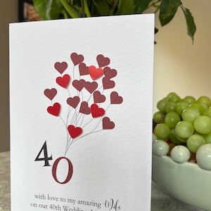 Puede incluir: Tarjeta blanca con un ramo de corazones rojos y granates, celebrando el 40 aniversario de bodas. La tarjeta dice: "con amor a mi maravillosa esposa en nuestro 40 aniversario de bodas".