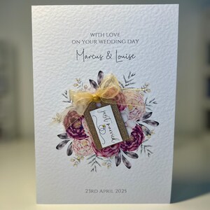 May include: A white wedding card with a floral design and a gold tag that says "just married". The card is addressed to Marcus & Louise and the date is 23rd April 2025.
