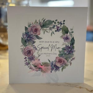 Muttertags-Blumenkranzkarte, handgefertigt und verziert mit winzigen Edelsteinen und Band. Hübsche rosa-fliederfarbene Karte. Besondere Mama. Muttertag Sonntag.