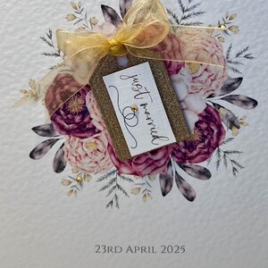May include: A white card with a floral design in shades of pink and purple. A gold glitter tag with the text "just married" is attached to the bouquet. The date "23RD APRIL 2025" is printed at the bottom of the card.