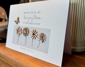 May include: A white card with the text "With love to an amazing Mum on Mother's Day" and a small butterfly and flowers with pink gems. The card also has the text "Mother's Day 2023".