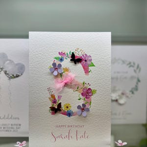 May include: A pink and white birthday card featuring a floral letter "S" and the text "Happy Birthday Sarah Kate".