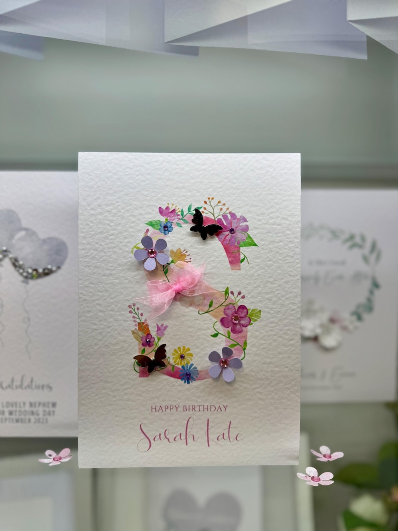 May include: A pink and white birthday card featuring a floral letter "S" and the text "Happy Birthday Sarah Kate".