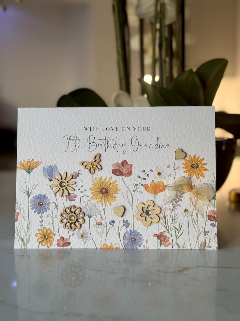 May include: A white card with a floral design and the text "With love on your 80th Birthday Grandma". The card has wooden flowers and hearts.