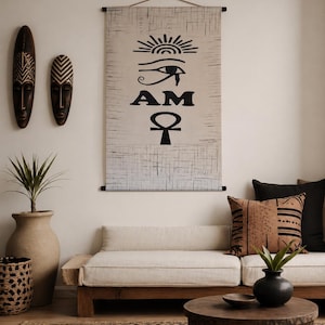 May include: A beige wall hanging with black hieroglyphic symbols and the word "AM". Two wooden masks and a large beige vase with a plant are on the wall. A wooden sofa with beige cushions and decorative pillows is in front of a round wooden coffee table.
