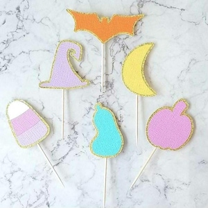 May include: Set of 7 Halloween themed cake toppers. The toppers are made of felt and feature a variety of designs, including a witch's hat, a bat, a candy corn, a pear, a crescent moon, and a pumpkin. The toppers are attached to wooden sticks.