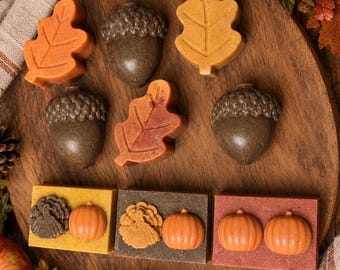 May include: A collection of autumn-themed soaps including three leaf-shaped bars in orange and red, two acorn-shaped bars in dark brown, and three rectangular bars featuring molded turkey and pumpkin designs in yellow, gray, and red.