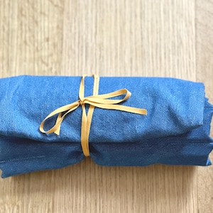 May include: A rolled-up, blue fabric item tied with a golden-yellow ribbon. The fabric appears to be a soft material, possibly linen or cotton. The ribbon is tied in a simple bow, suggesting a gift or presentation.