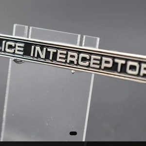 Puede incluir: Llavero de plata con una etiqueta rectangular negra que dice "POLICE INTERCEPTOR".