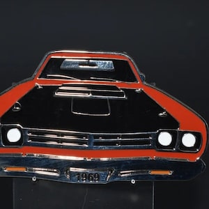 May include: A red and black metal keychain shaped like a 1969 Plymouth Road Runner car. The keychain has a silver finish and the car has white headlights. The keychain has a metal ring for attaching keys.
