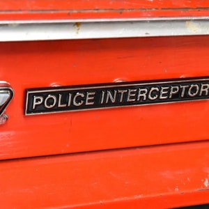Peut inclure: Gros plan sur une boîte à outils rouge avec un emblème "Police Interceptor" argenté et noir.