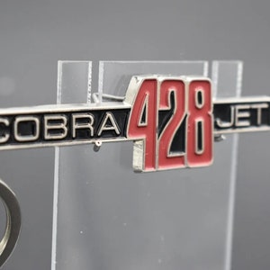 May include: A silver key chain with a black and red metal charm that says "COBRA 428 JET".