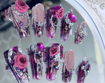 May include: Set of ten coffin-shaped false nails with intricate designs. Each nail features a pink rose, rhinestones, and silver chains. The nails are painted in shades of purple and pink.