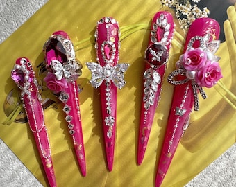 May include: Five long, pink acrylic nails with intricate designs. Each nail features rhinestones, silver accents, and a different design, including a butterfly, a flower, and a bow.