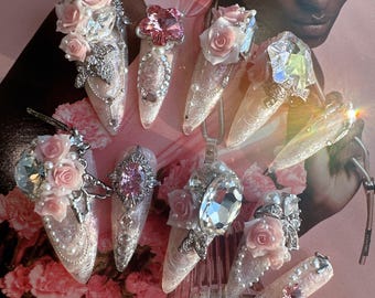May include: Close-up of ten long, pointed, white, sparkly, false fingernails with pink and white flowers, rhinestones, and silver accents.