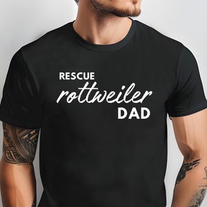 K&ouml;nnte beinhalten: Ein schwarzes T-Shirt mit wei&szlig;em Text, der "Rescue Rottweiler Dad" lautet.