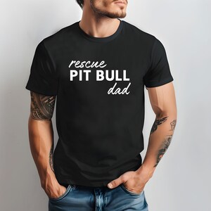 May include: Black t-shirt with white text that reads "rescue pit bull dad".
