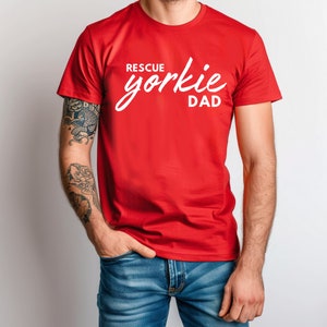 Op de afbeelding: Een rood T-shirt met de tekst "RESCUE yorkie DAD" in witte letters.
