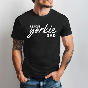 Op de afbeelding: Een zwart T-shirt met witte tekst die "Rescue yorkie DAD" zegt.