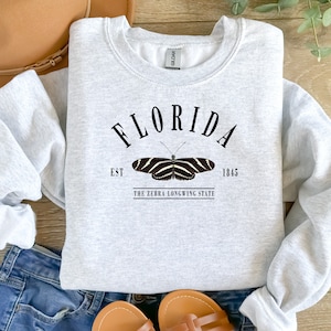 May include: Gray sweatshirt with a black graphic design that says "FLORIDA EST. 1845 THE ZEBRA LONGWING STATE" with a black and white butterfly illustration.