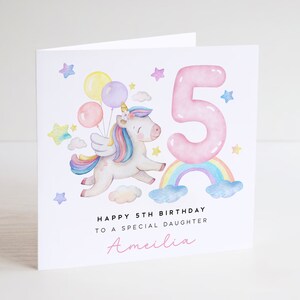 May include: A pink and white unicorn with a rainbow and a pink number 5. The unicorn is holding balloons and flying in the air. The text says "Happy 5th Birthday to a special daughter Amelia".