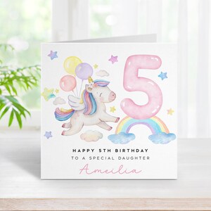 May include: A white card with a pink unicorn flying with balloons over a rainbow. The card says "Happy 5th Birthday to a special daughter Amelia".