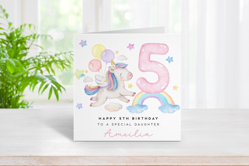 May include: A white card with a pink unicorn flying with balloons over a rainbow. The card says "Happy 5th Birthday to a special daughter Amelia".