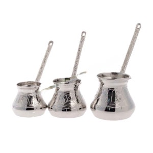 Könnte beinhalten: Drei silberne türkische Kaffeekannen mit verzierten Designs. Die Kannen sind in verschiedenen Größen und haben lange Griffe.