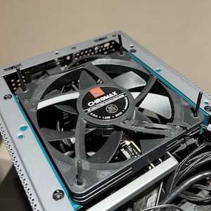 May include: A black computer case fan with a silver grill and a black label that reads "CHROMA MAX WF-A12C215 PWM Chromatic Ultra Silent 6.13A 1.56W DC12V".