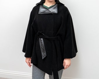 May include: A black wool cape with a black leather collar and a black leather belt. The cape has a single button closure.