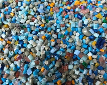 Könnte beinhalten: Nahaufnahme eines Haufens bunter Kunststoffgranulate. Die Granulate sind klein und zylindrisch und in verschiedenen Farben, darunter Blau, Grün, Gelb und Braun.