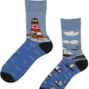 May include: A pair of blue socks with a nautical theme. One sock features a red and white lighthouse on a small island with blue water and white waves. The other sock features a blue sky with white clouds and several white sailboats on blue water with white waves.