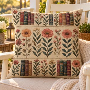 May include: A square throw pillow with a beige background featuring a repeating pattern of vertical rows. The design includes illustrations of colorful flowers and antique book spines arranged in horizontal bands across the fabric surface.