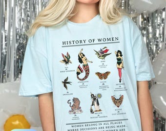 Puede incluir: Camiseta azul claro con un estampado gráfico de varias figuras femeninas y el texto "HISTORY OF WOMEN". El texto debajo del gráfico dice "WOMEN BELONG IN ALL PLACES WHERE DECISIONS ARE BEING MADE... IT SHOULDN'T BE THAT WOMEN ARE THE EXCEPTION."