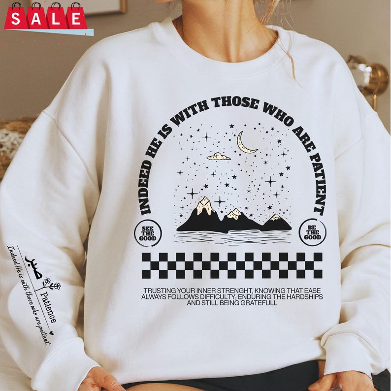 K&ouml;nnte beinhalten: Wei&szlig;er Pullover mit einem schwarzen Grafikdesign, das eine Sichelmond, Sterne, Berge und den Text "Indeed He is with those who are patient." zeigt. Die Grafik enth&auml;lt auch zwei kleine Quadrate mit dem Text "See the good" und "Be the good". Der Text unter der Grafik lautet "Trusting your inner strength, knowing that ease always follows difficulty, enduring the hardships and still being grateful."