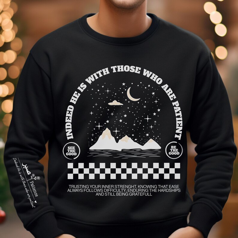 K&ouml;nnte beinhalten: Schwarzer Pullover mit einem wei&szlig;en Grafikdesign, das eine Sichelmond, Sterne, Berge und den Text "Indeed he is with those who are patient." zeigt. Die Grafik ist von einem karierten Muster umgeben. Der Text "See the good" und "Be the good" sind ebenfalls im Design enthalten. Der Text unter der Grafik lautet "Trusting your inner strength, knowing that ease always follows difficulty, enduring the hardships and still being grateful."