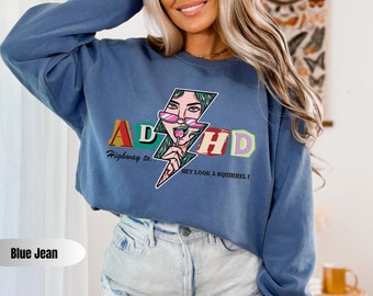May include: Blue jean sweatshirt with a graphic of a woman with pink sunglasses and a lollipop. The graphic says "ADHD Highway to... Hey Look a Squirrel!"