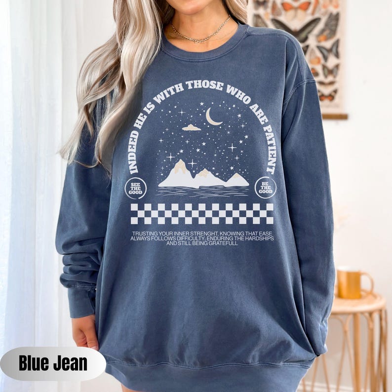 K&ouml;nnte beinhalten: Ein blaues Langarmshirt mit einem wei&szlig;en Grafikdesign, das eine Sichelmond, Sterne, Berge und den Text "Indeed he is with those who are patient." zeigt. Die Grafik enth&auml;lt auch den Text "See the good" und "Be the good" in zwei Kreisen.