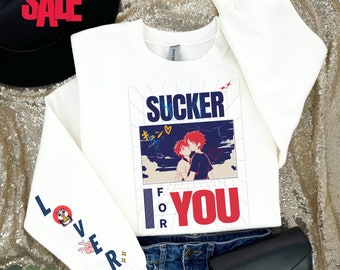 May include: White sweatshirt with the text "SUCKER FOR YOU" in blue and red, with an anime-style illustration. The left sleeve has the word "LOVER" and a cartoon character. The sweatshirt is paired with blue jeans and a black clutch.