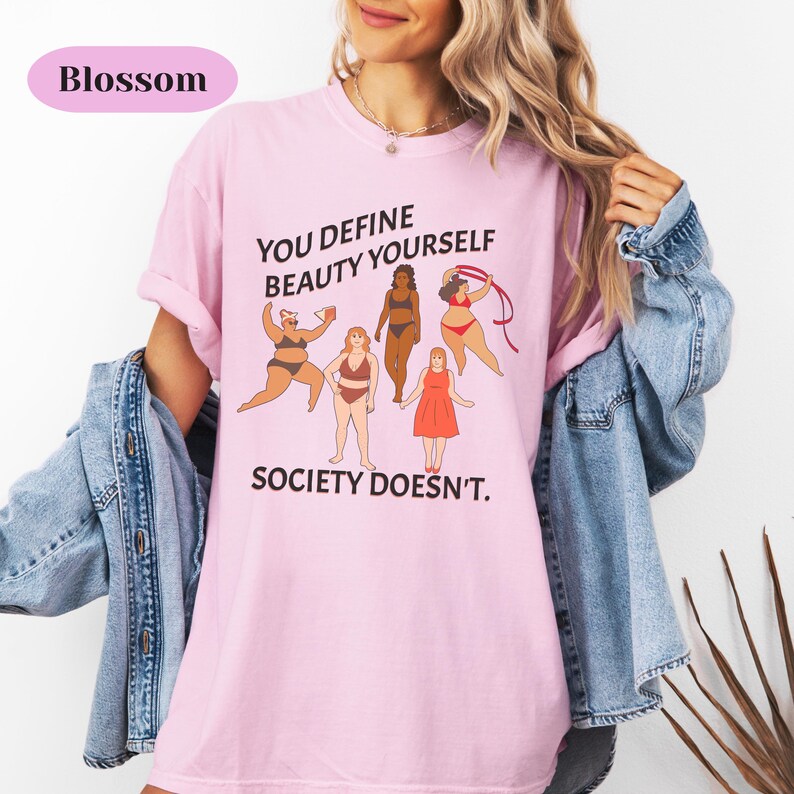 K&ouml;nnte beinhalten: Pinkes T-Shirt mit einem Grafikdruck von verschiedenen Frauen und dem Text "You define beauty yourself, society doesn't."
