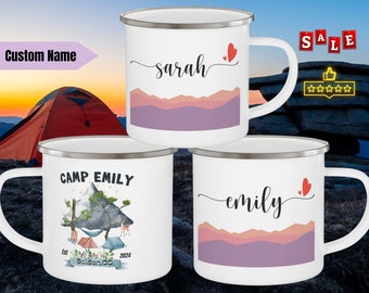 May include: Three white enamel camping mugs with different designs. The first mug has the name "sarah" written in cursive with a red heart. The second mug has the text "CAMP EMILY" with a mountain scene and the text "Est. 2024" and "golden.co". The third mug has the name "emily" written in cursive with a red heart.