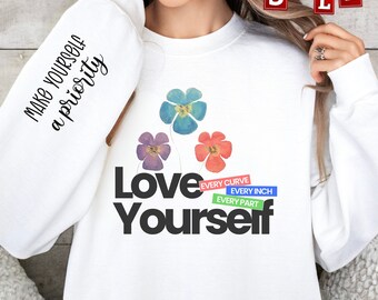 May include: White sweatshirt with the text "Make yourself a priority" on the sleeve and "Love Yourself" with the words "Every Curve, Every Inch, Every Part" underneath on the front. The sweatshirt has a graphic of three watercolor flowers.
