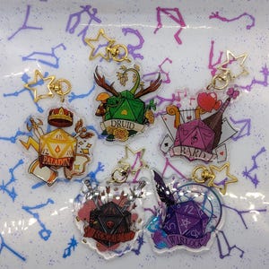 Può includere: Cinque portachiavi in acrilico con temi di classe di Dungeons & Dragons. Ogni portachiavi ha una chiusura dorata a forma di stella. I disegni includono un Paladino, Druido, Bardo, Ladro e Warlock, ognuno con illustrazioni uniche e nomi di classe.