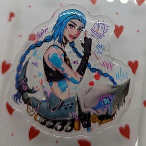 Pode incluir: Um alfinete transparente de resina com um personagem de cabelo azul com tatuagens azuis, usando um top preto e luvas sem dedos. O alfinete tem a palavra "Jinx" e "HA HA" escrita, com uma arma estilizada.