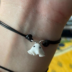 Op de afbeelding: Een zwarte armband van touw met een witte spookbedel. Het spook heeft twee zwarte ogen.