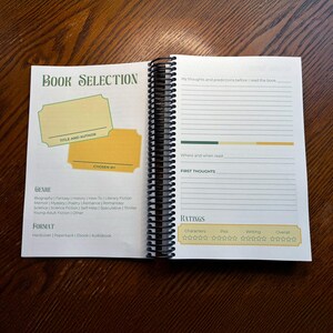 May include: A book selection journal with a green and yellow colour scheme. The journal has sections for book title and author, genre, format, chosen by, my thoughts and predictions before I read the book, where and when read, first thoughts, and ratings. The ratings section has five stars for characters, plot, writing, and overall.