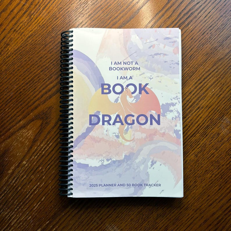 May include: A spiral bound planner and book tracker with a watercolor background. The cover features a dragon with the text "I am not a bookworm I am a book dragon" and "2025 Planner and 50 Book Tracker".