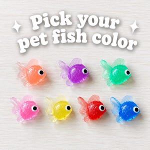 May include: Seven small, translucent plastic fish figurines with googly eyes, arranged in two rows. The fish are colored orange, purple, green, pink, yellow, red, and blue. The text "Pick your pet fish color" is printed in white above the fish.