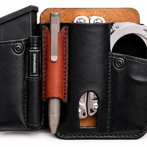 May include: Black leather multi-tool organizer with a brown leather pen holder. Includes a magazine pouch, a pen with "SERAPHINKS" printed on it, a multi-tool, and handcuffs. The organizer is designed to hold various tools and accessories.